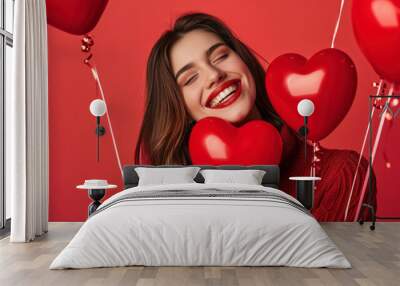 Happy girl celebrating Valentine`s Day, young woman model and heart shape balloons on red studio background, romantic design. Concept of love, party, fun, smiling people Wall mural